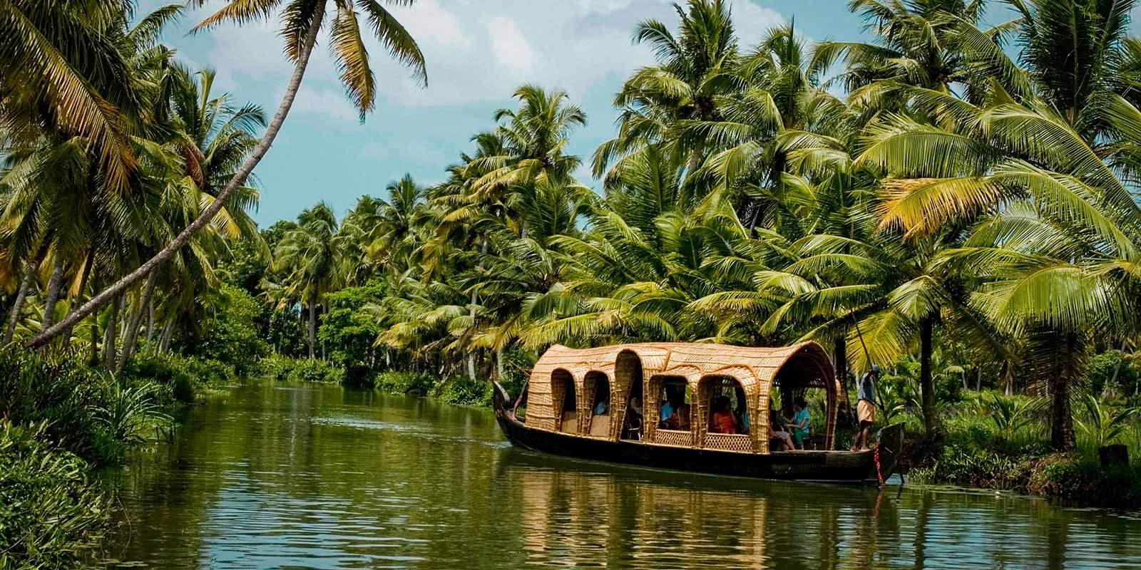 A-boat-floats-on-a-river-surrounded-by-lush-coconut-trees-at-Coconut-Lagoon-Retreat-in-India.jpg