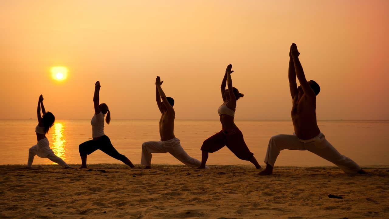 A-group-of-people-practicing-yoga-on-the-beach-at-sunset-representing-the-Yoga-Kushti-Akharas-of-Varanasi.jpg