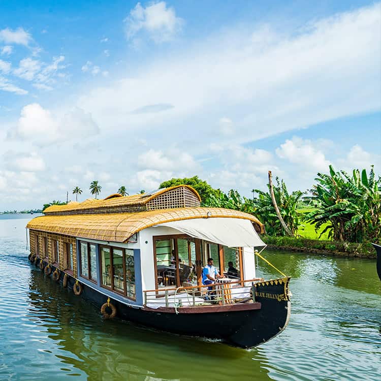 A houseboat with people on board floating on the water at Coconut Lagoon Retreat in India A houseboat with people on board floating on the water at Coconut Lagoon Retreat in India