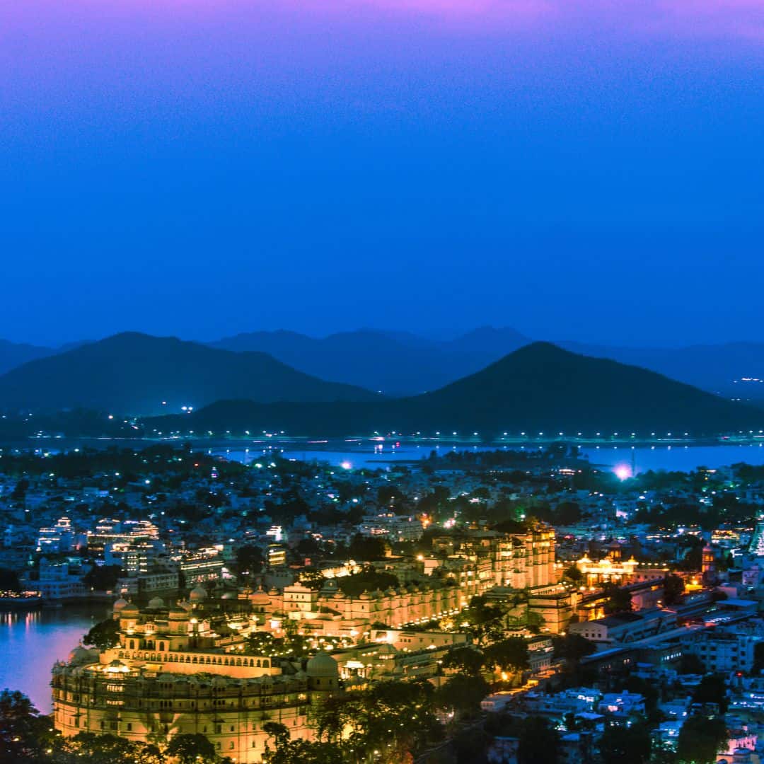 A nighttime panorama of Udaipur, India, highlighting the city's lights and picturesque lakes under a dark sky A nighttime panaroma of Udaipur India highlighting the city's lights and picturesque lakes under a dark sky