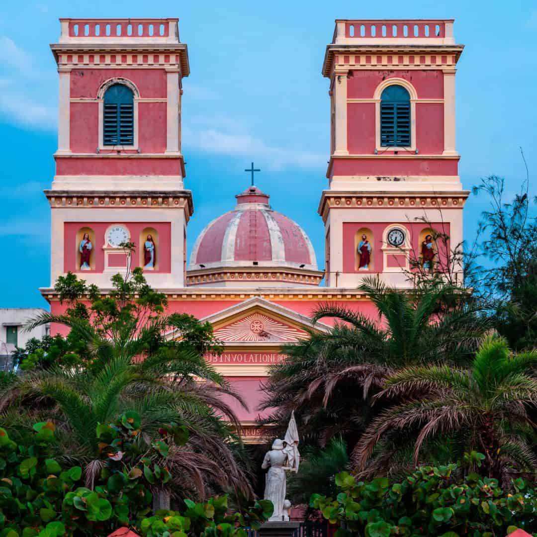 A pink church with two towers surrounded by palm trees, located in Pondicherry A pink church with two towers surrounded by palm trees located in Pondicherry