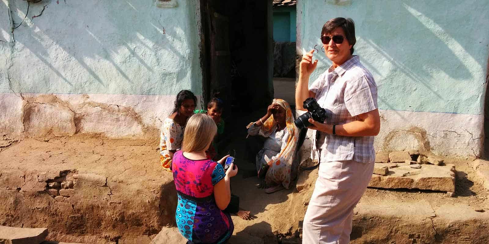 A-woman-holding-a-camera-stands-in-front-of-a-house-in-Chanoud-Garh-India-capturing-the-scene.jpg