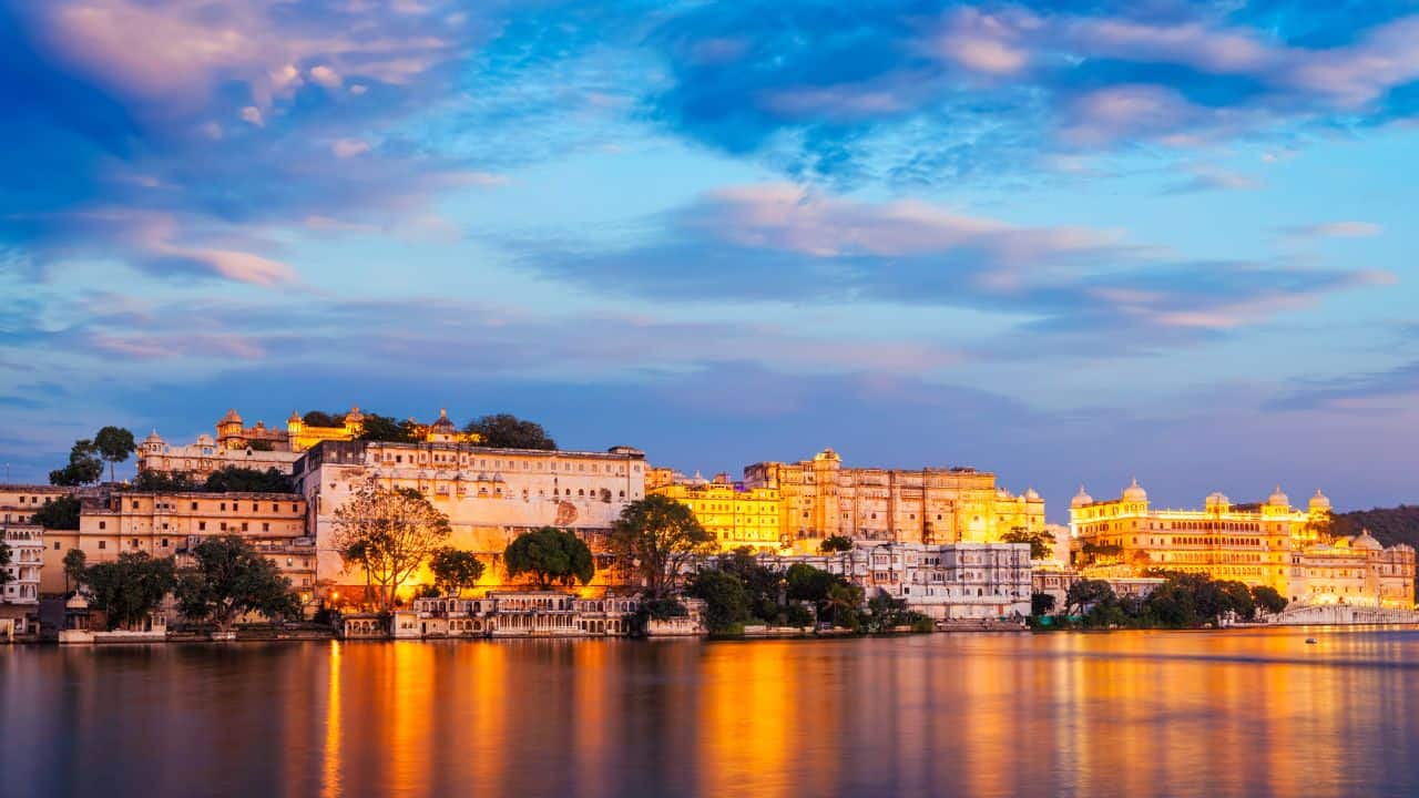 Evening-in-Udaipur-India-with-the-city-lights-shimmering-on-the-water-and-a-vibrant-sunset-illuminating-the-sky.jpg