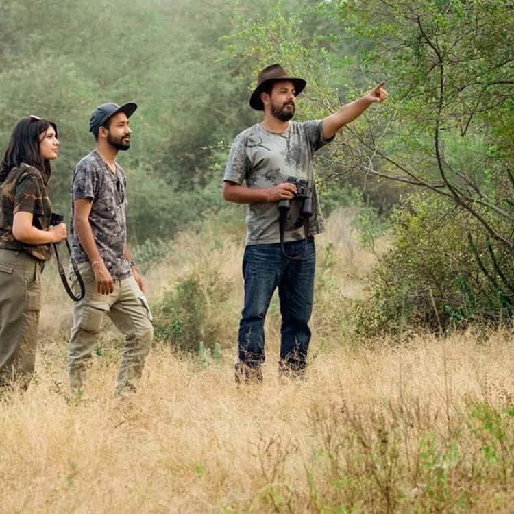 Three people in a Rajasthan field, with a man pointing at something in the distance, surrounded by nature and wildlife Three people in a Rajasthan field, with a man pointing at something in the distance, surrounded by nature and wildlife