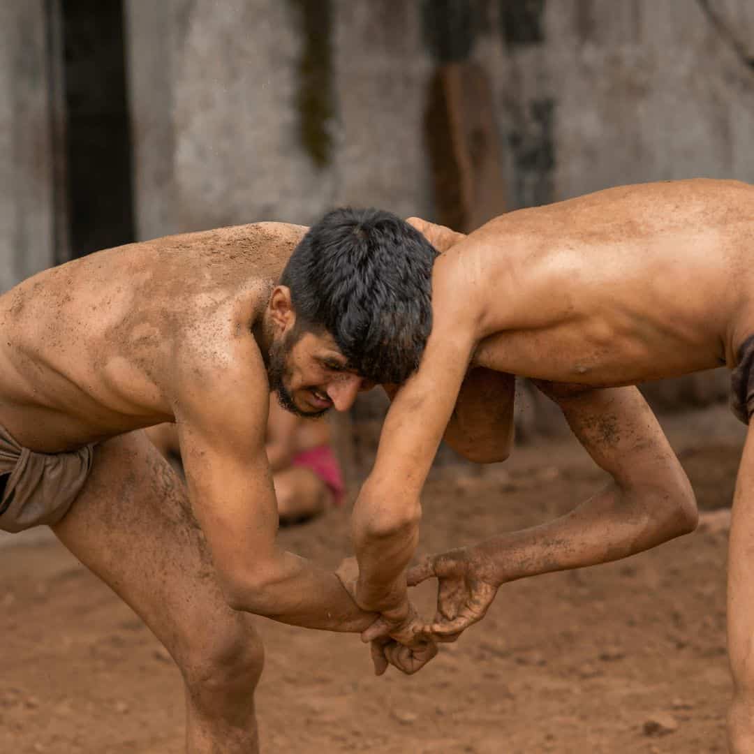 Two men engaged in Kushti wrestling, grappling in the dirt, showcasing traditional wrestling techniques in Varanasi Two men engaged in Kushti wrestling grappling in the dirt showcasing traditional wrestling techniques in Varanasi