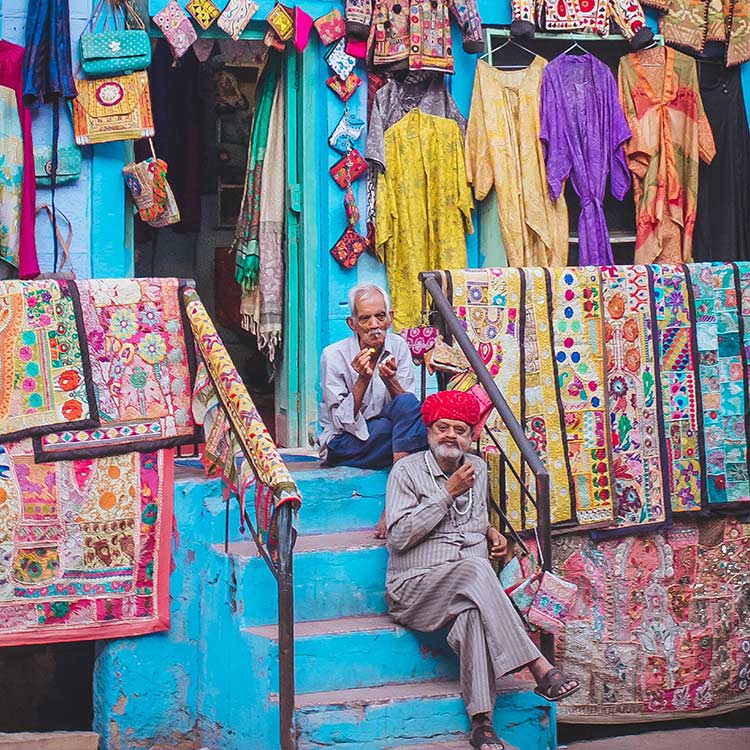 Two men are seated on steps in front of a colorful shop in India, highlighting the vibrant street life and commerce Two men are seated on steps in front of a colourful shop in India highlighting the vibrant street life and commerce